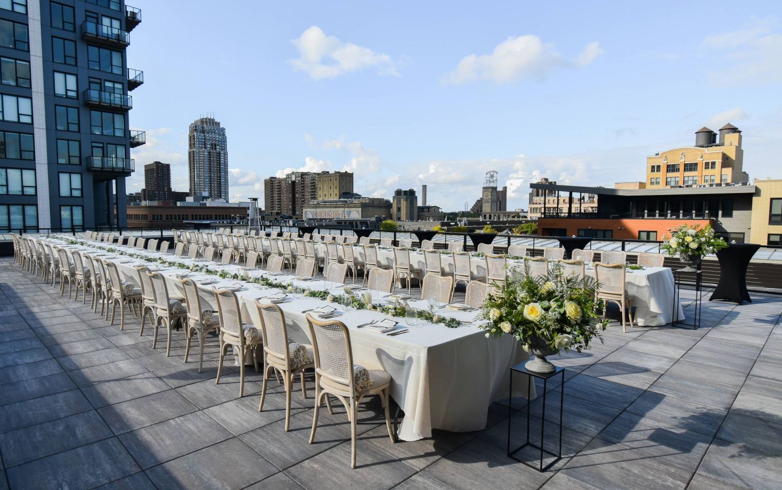 The rooftop of JI Case presents an arranged dining area for an event, featuring elegant table settings and panoramic city views.